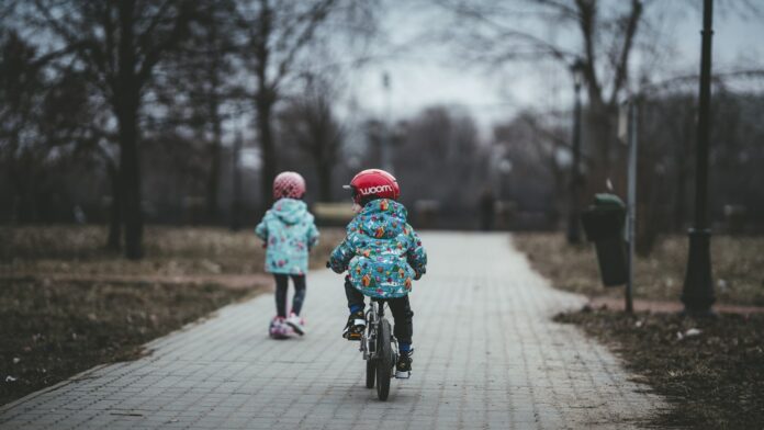 child riding with bike and another child walking on concrete pavement near trees