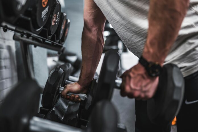 Photo by Anastase Maragos person in gray shirt holding black dumbbell